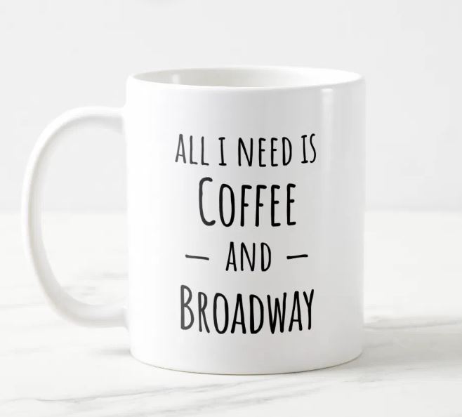 A white coffee mug with the text "all I need is coffee and Broadway"