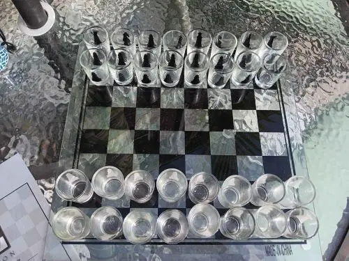 A glass chess board with shot glasses as chess pieces