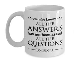 A coffee mug with text "He who knows all the answers has not been asked all the questions"