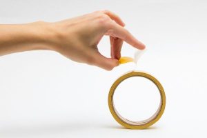 A hand holding a roll of double sided adhesive tape