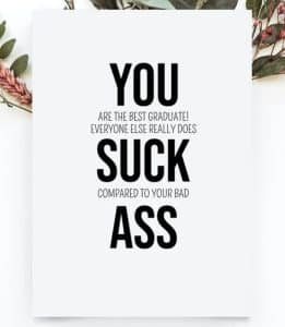 Funny graduation message card with YOU SUCK ASS in capital letters and a smaller hidden graduation message in the middle