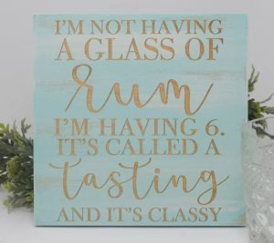 A wooden sign with "I'm not having a glass of rum, I'm having 6 and it's called a tasting and it's classy"