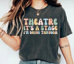 A woman wearing a shirt with "theatre it's a stage I'm going thorugh"