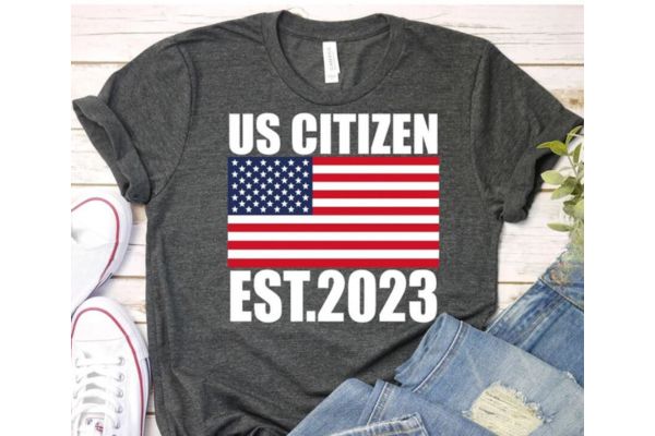 A grey t-short with the US flag and "US citizen est. 2023"